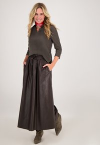 Bruine leren maxi rok met elastische tailleband en zakken, gecombineerd met een aansluitend olijfgroen top en een rode gebloemde sjaal.