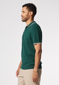 Polo de manga corta verde con un diseño de cuadros texturizado, con cuello y puños en contraste blanco, y una silueta ajustada.