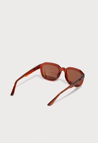 Gafas de sol tintadas en rojo con un marco grueso y angular. Presentan lentes marrones oscuros y patillas rectas y elegantes. Acabado brillante.