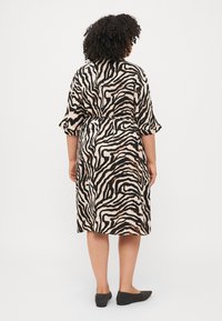 Kostiumėlis su béžine baze ir juodais zebro raštais, turintis trumpas rankoves, laisvą siluetą ir kelių ilgio apdailą. Dėvimas su juodais butais.