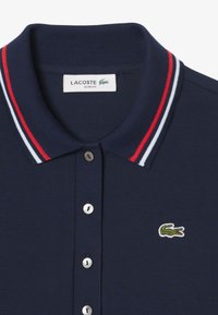 Navy blue slim-fit polo shirt with a ribbed collar featuring red and white stripes. Includes three buttons and a green embroidered crocodile logo.
