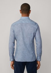 Camisa de manga larga azul con un patrón, cuello clásico, puños con botón y un dobladillo ligeramente curvado. La tela tiene una textura suave.