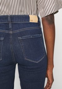 Mörkblå denimjeans med hög midja, som har en tan läderetikett, sömnad på bakfickan och tapered bendesign.