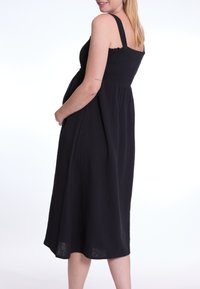 Schwarzes, ärmelloses Kleid mit einem rüschierten Oberteil und legerem Schnitt. Hergestellt aus leichtem Stoff, hat es einen knielangen Saum und eine subtile Textur.