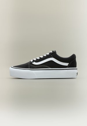 Czarny niski sneaker z białym bocznym paskiem, białymi sznurowadłami i grubą białą gumową podeszwą na neutralnym tle.