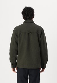Olijfgroene wollen jas met een kraag, knopenmanchetten en een detail aan de achterkant, met een ontspannen pasvorm en een zachte textuur.
