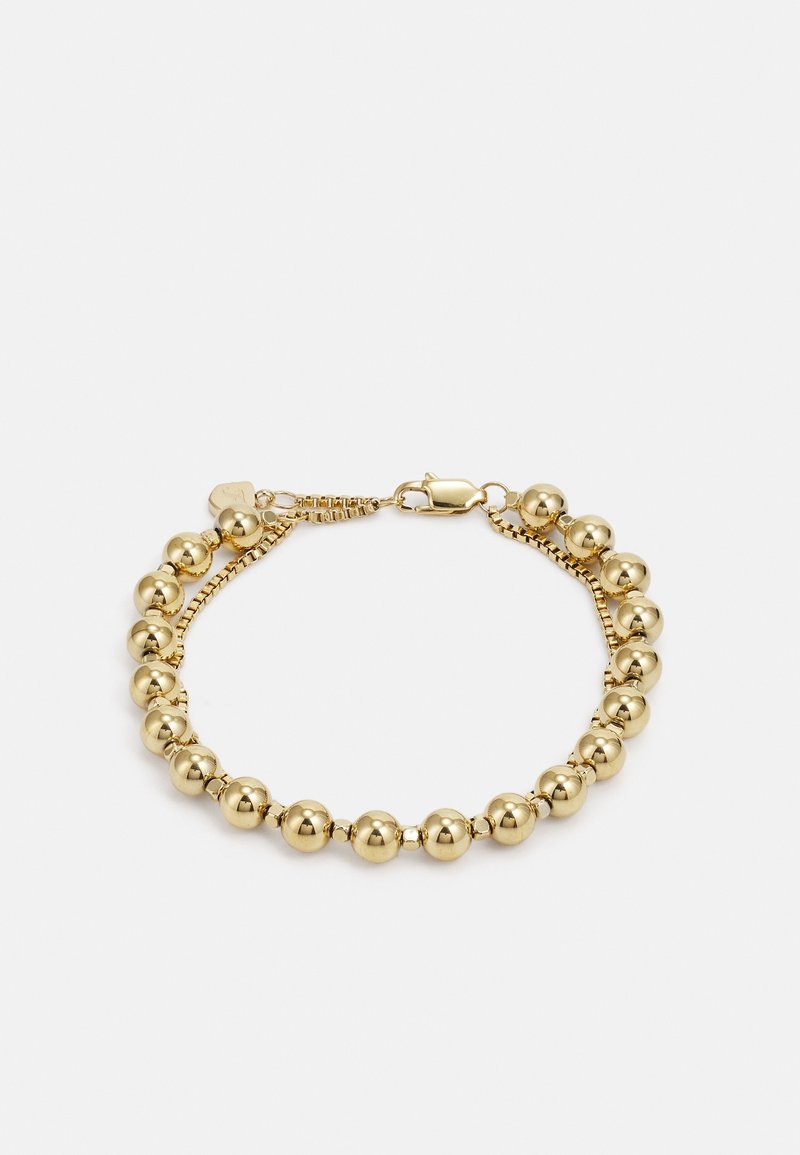 Bracelet ton or avec de grosses perles rondes poliess et un fermoir mousqueton sur fond blanc.