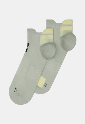 Svetlo zelene nogavice z rebrasto teksturo, rumenimi poudarki na manšetah in kontrastnim logotipom. Vsaka nogavica ima okrepljen peto in prste.