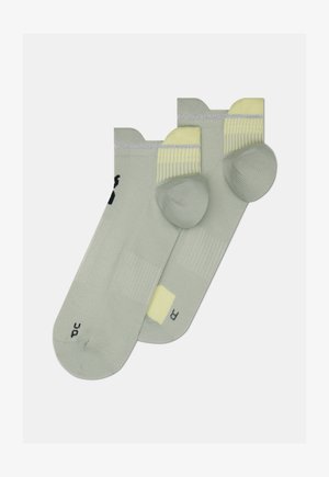 Svetlo zelene nogavice z rebrasto teksturo, rumenimi poudarki na manšetah in kontrastnim logotipom. Vsaka nogavica ima okrepljen peto in prste.