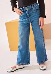 Jean en denim bleu évasés avec une poche avant et un bouton en métal, associés à des ballerines argentées avec des accents de sangle.