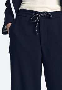Sötétkék széles szárú nadrág sima anyagból, húzózsinóros derékkal, kontrasztos fehér részletekkel és elülső zsebbel.