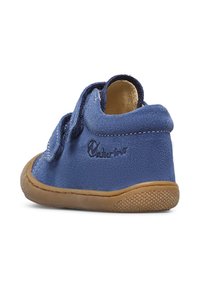 Zapato de gamuza azul con suela de goma marrón, que cuenta con una correa de velcro y detalles de costura. Logo visible en el lateral. Diseño de punta redonda.