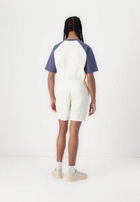 Outfit casual que incluye una camiseta blanca de manga corta con mangas azules y pantalones cortos de textura clara, combinados con zapatillas de colores neutros.