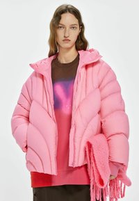 Roze gewatteerde jas met een doorgestikt ontwerp, capuchon en ritsluiting. Gelaagd over een gradient trui; houdt een pluizige roze sjaal met franjes vast.