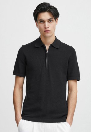 Svart kortermet polo-skjorte med en myk ribbestruktur, som har glidelås og en klassisk kragedesign.