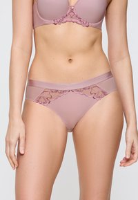 Světle růžové krajkové spodní prádlo s hladkým pasem, zdobené složitými květinovými akcenty a texturovaným designem látky.