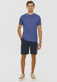 Niebieska bawełniana koszulka, dopasowany krój. Czarne szorty o standardowym kroju. Jasnoszare trampki ze sznurówkami. Prosty, codzienny strój.