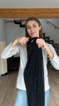 Black fabric scarf with white dot pattern, loose design, soft texture. Model holds it in front of a light-colored, modern interior.