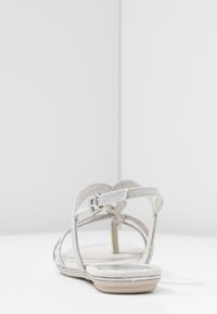 Hopeinen hihnallinen sandaali, jossa on tasapohja, hienostuneet hihnat kimaltelevilla yksityiskohdilla ja takana soljellinen kiinnitys.
