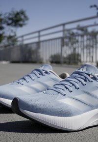 Helleblaue Laufschuhe mit einem strukturierten Mesh-Obermaterial, weißen Akzenten und einer schwarzen Gummisohle. Verfügen über ein Schnürdesign und auffällige Markenkennzeichnung.