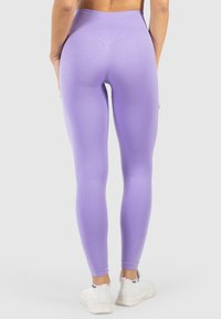 Różowe legginsy z wysokim stanem wykonane z elastycznego materiału, z gładką fakturą i dopasowanym krojem. Widok z tyłu, w połączeniu z białymi sneakersami.