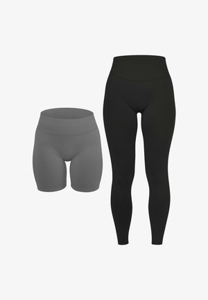 Frau trägt hoch taillierte schwarze Leggings und weiße Sneakers, steht mit den Armen entspannt an den Seiten vor einem schlichten Hintergrund.