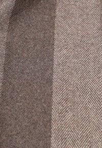 Houndstooth-patterned fabric in brown and beige, featuring textured wool with a smooth finish and subtle color variations.