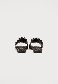 Sandales plates noires avec un imprimé animal texturé, dos ouvert et piques décoratives le long des lanières. Semelle intérieure douce avec une marque discrète.