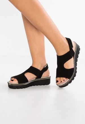 Czarne sandały na platformie z zamszu, z odkrytymi palcami, elastycznymi paskami i srebrnym przeszyciem wzdłuż podeszwy. Widoczna fakturowana czarna gumowa podeszwa.