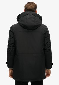 Chaqueta de invierno acolchada negra con capucha, con una textura suave, puños ajustables y un logotipo en relieve en la parte superior de la espalda.