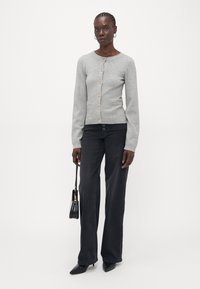 Light gray cardigan with a round neck, front buttons, and a textured finish. Paired with black wide-leg pants and a small black handbag.