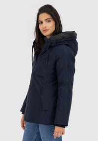 Giacca con cappuccio blu navy con zip frontale, tasche laterali e una superficie liscia. Presenta dettagli neri e stringhe elastiche.