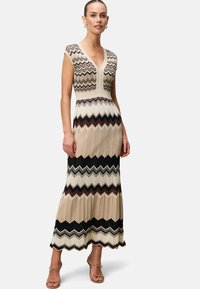 Maxi dress with a chevron pattern in beige, brown, and black. Features a V-neck, cap sleeves, and a fitted waist that flares at the hem.