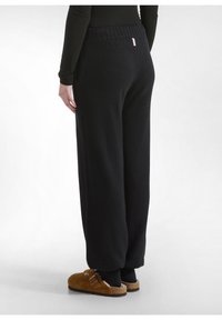 Zwarte, losvallende broek met een geribbelde tailleband en een zachte textuur. Opvallend kenmerk is een klein logo-label aan de achterkant.