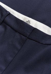 Pantalons bleu marine en tissu lisse, avec une ceinture intérieure blanche portant une étiquette logo, et des coutures nettes sans embellissements.
