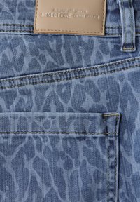 Jean en denim bleu avec un motif subtil d'imprimé animal, comprenant des coutures visibles et un patch de marque en cuir beige à la taille.