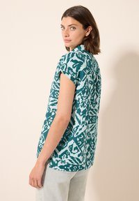 Maglietta a maniche corte color teal con un motivo astratto in azzurro chiaro a contrasto, realizzata in un tessuto leggero, con una vestibilità comoda e orlo arrotondato.