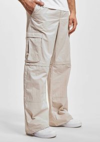 Pantalons cargo beige avec une coupe ample, dotés de poches latérales, d'une texture lisse et d'un design droit. Associés à des chaussures blanches.