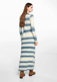 Pitkä neulemekko, jossa on sinisiä ja kermaa vaakasuoria raitoja, hoikka siluetti, pyöreä pääntie ja pitkät hihat. Yhdistetty ruskeisiin nilkkasaappaisiin.