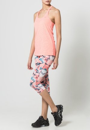 Roze lichte tanktop en bedrukte capri-legging in pastelkleuren met geometrische ontwerpen, gecombineerd met zwarte sport schoenen.