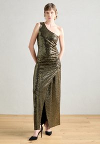 Robe à une épaule en sequins dorés avec une fente sur le côté, au design épuré et ajusté, et à la texture douce, associée à des chaussures à talons hauts noires.