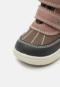 Chaussure d'enfant marron et noire avec des sangles en velcro, semelle en caoutchouc et couture contrastante. Bout rond, tissu texturé et accents sur les côtés.