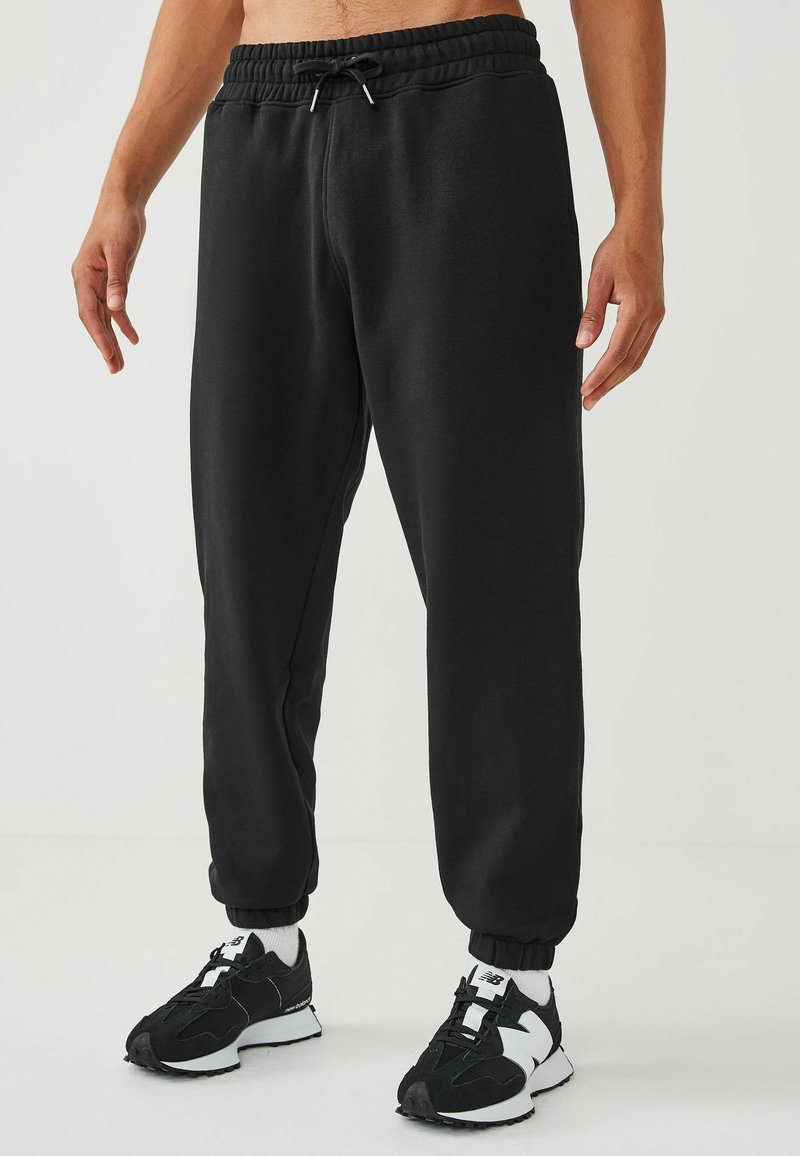 Pantalones de chándal negros hechos de tela suave, con una cintura elástica y cordón, y puños ajustados en los tobillos.