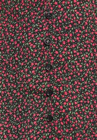 Gros plan d’un tissu noir avec de petites fleurs rouges, des feuilles vertes, des points blancs et une rangée verticale de cinq boutons noirs.