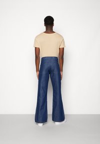 Beige t-shirt med rund hals och högmidjade blå denim byxor med utställda ben, med en mjuk textur, stora bakfickor och vita sneakers.