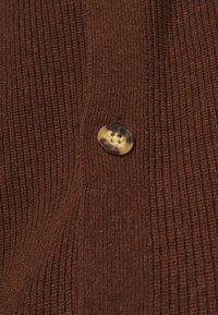 Gros plan sur un tissu tricoté côtelé marron avec un bouton rond, à quatre trous, marbré marron et beige, cousu.