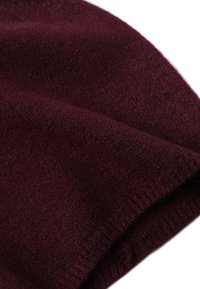 Un material tricotat moale, de culoare burgundă, cu textură vizibilă și fibre fine, evidențiind o margine pliată pe un fundal alb.
