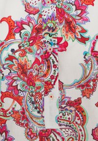 Vit skjorta med färgglad blommig och paisleytryck i röd, rosa, grön och blå. Har två knappar och ett mjukt, texturerat tyg.