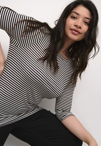 Top a rayas blanco y negro con mangas tres cuartos y escote redondo, combinado con pantalones negros. Tejido ligero y diseño ajustado.