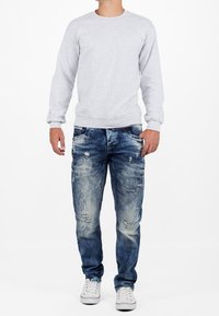 Gray crewneck sweatshirt, blue distressed jeans, white sneakers; casual style with ribbed cuffs and multiple pockets on jeans.